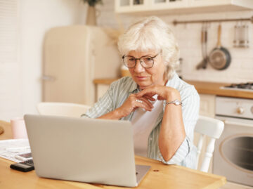 modern technology old people retirement gray haired female pensioner glasses filling loan application form online sitting front laptop reading information with serious focused look scaled