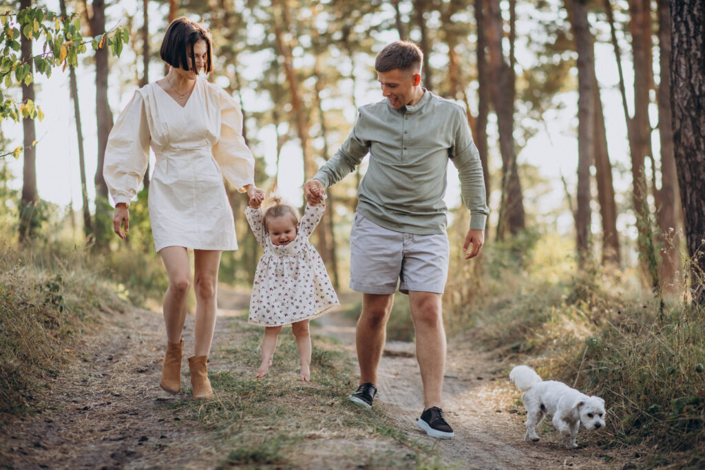 young family with cute little daughter walking forest sunset